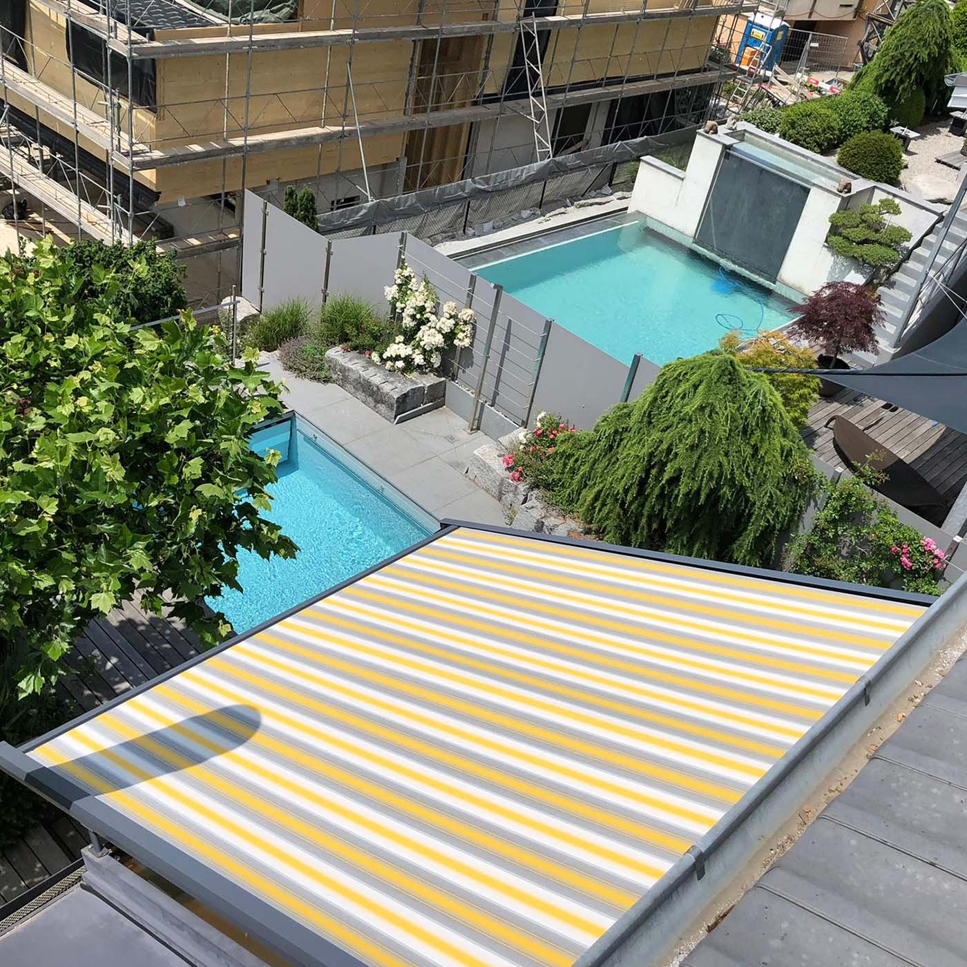 Gelenkarmmarkise mit gelb-weiss gestreiftem Tuch, von oben über einer Terrasse ausgefahren