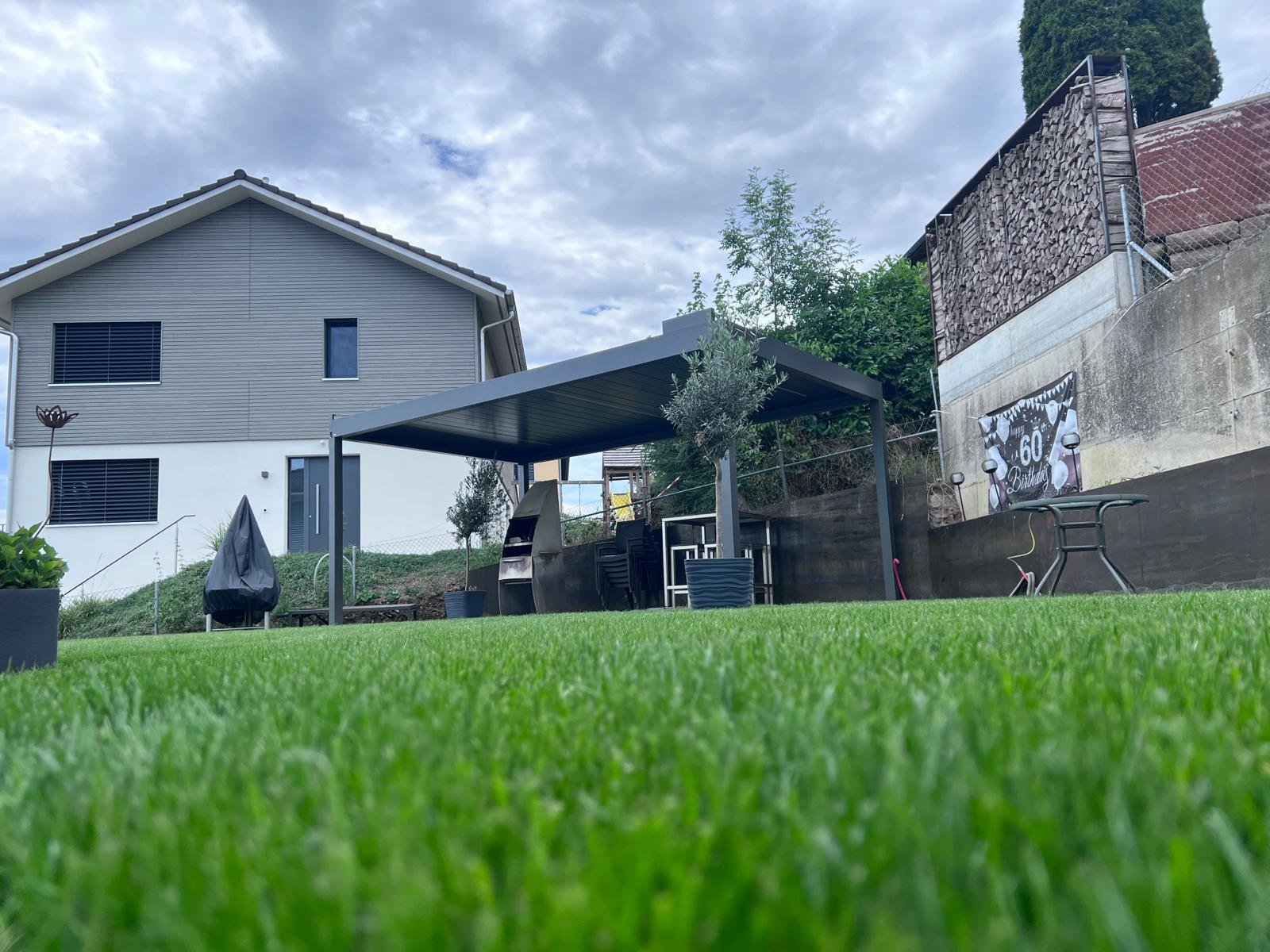 Freistehendes Terrassendach in einem Garten, davor eine Rasenfläche