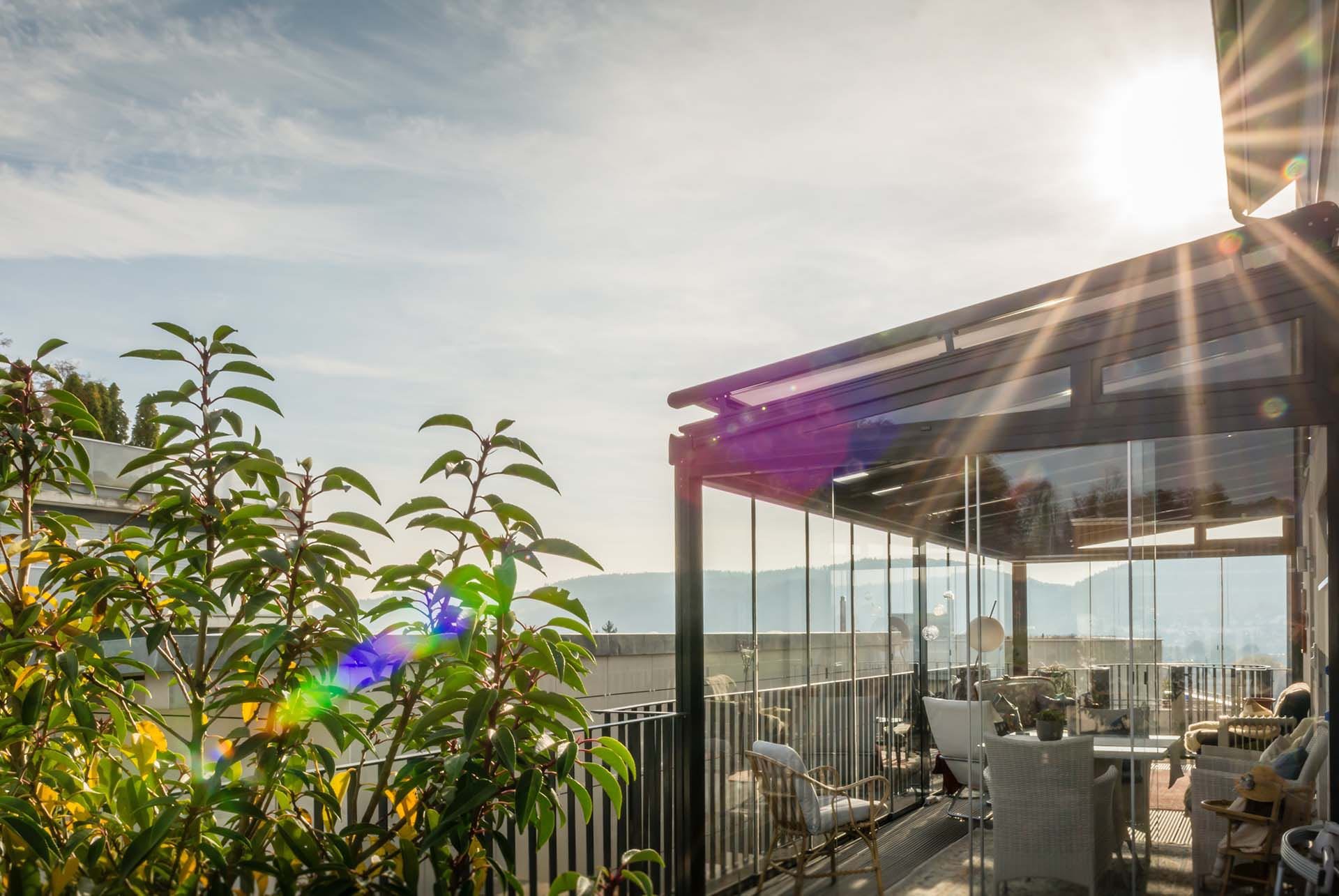 Terrassendach mit Glasdach und seitlichen Glaselementen, von der tiefstehenden Sonne durchleuchtet