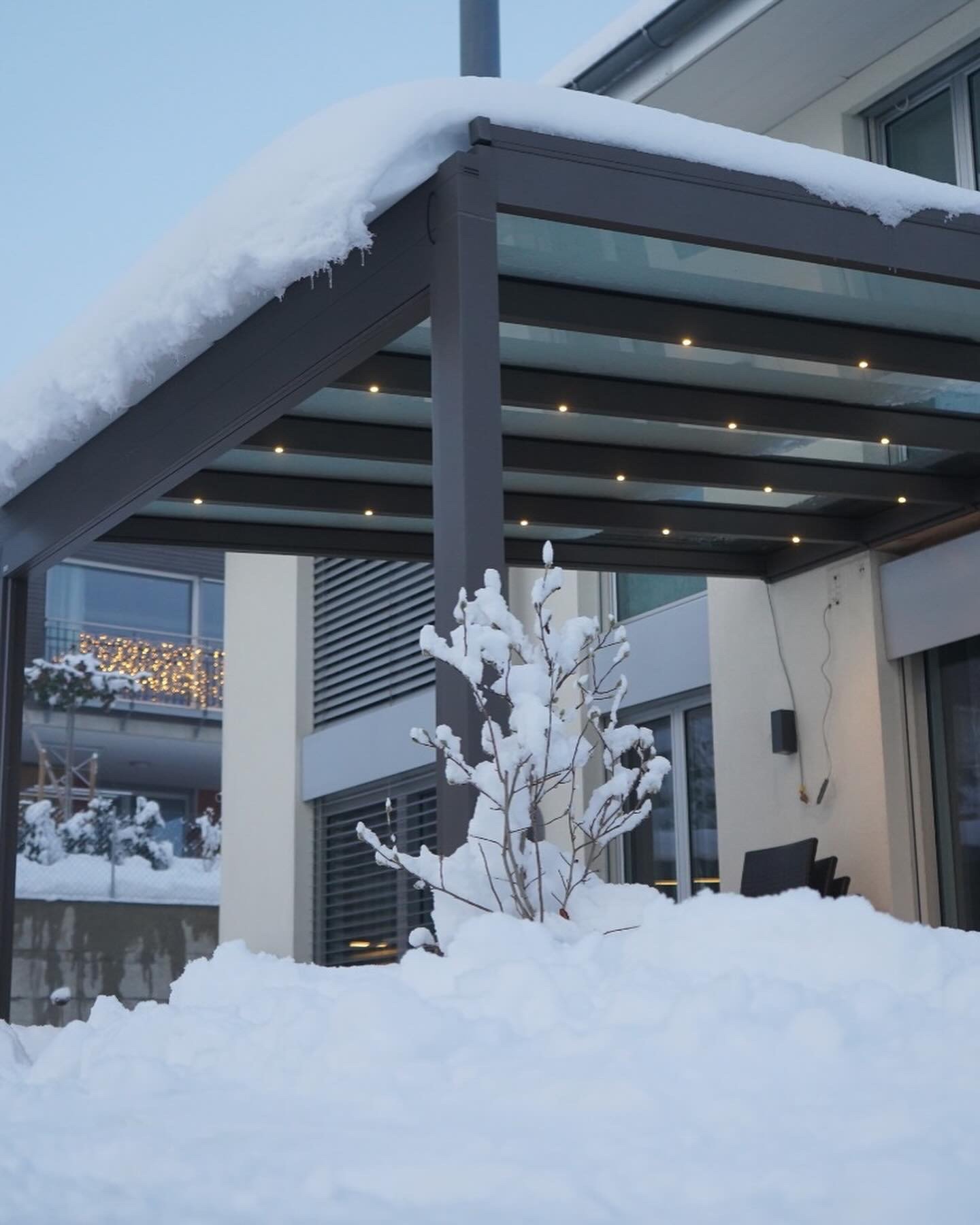 Terrassendach mit Glasdach unter einer Schneeschicht, darunter beleuchtete Terrasse