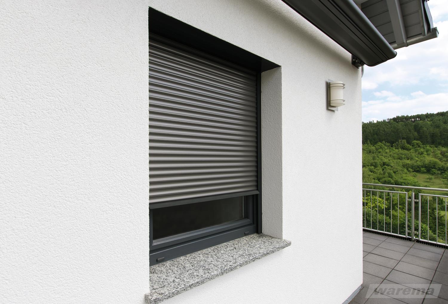 Grauer Rollladen, halb heruntergelassen, an einem Fenster mit Granitsims