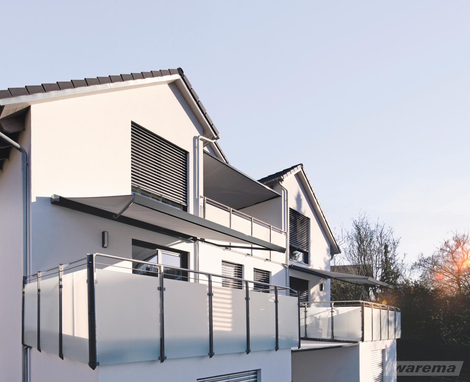Wohnhaus mit Lamellenstoren an den Fenstern und ausgefahrenen Markisen über den Balkonen